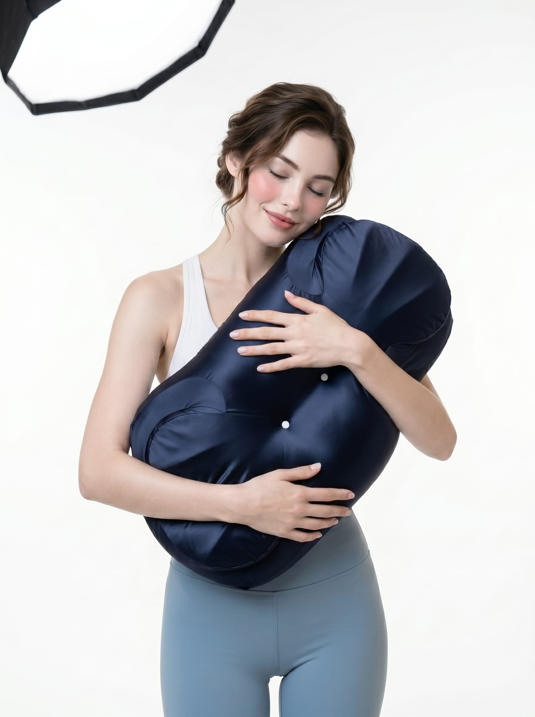 A woman holding the navy AIjia Shell Pillow close against her, eyes closed and smiling